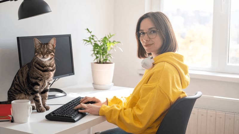 デスクの前に座っている白人女性と、デスク上の猫